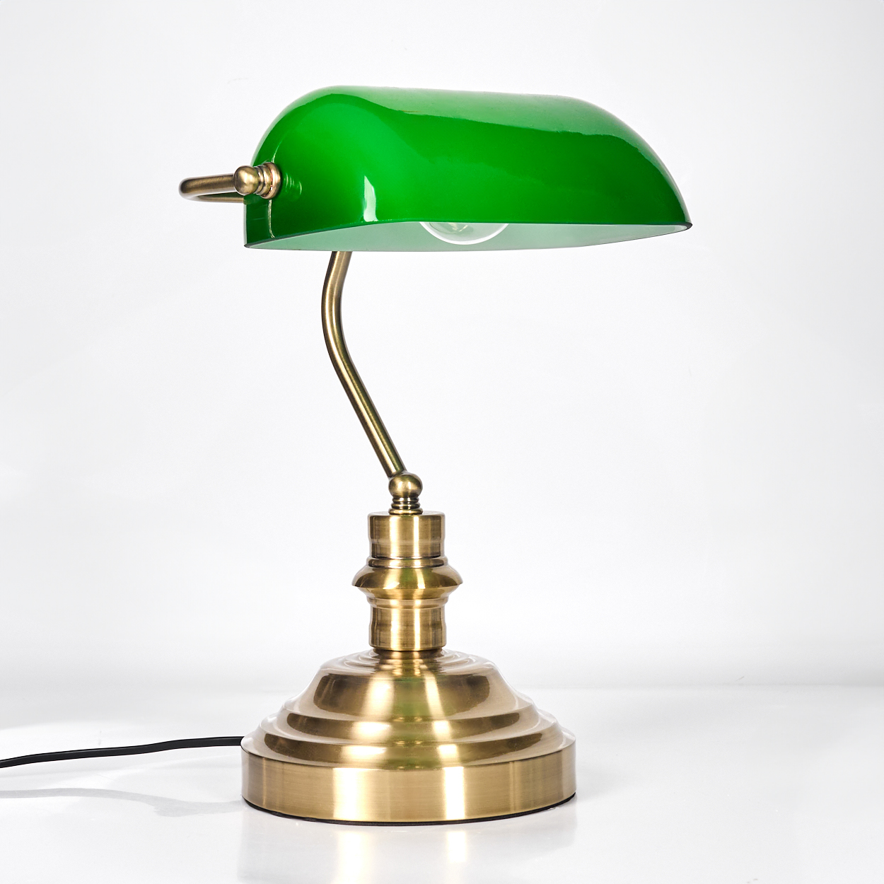 Eine grüne Banker-Lampe mit Messingfuß und -arm, vor weißem Hintergrund. Die Lampe ist an.