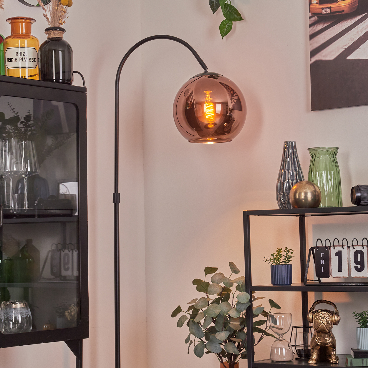 Eine Zimmerecke mit Lampe, Regalen, Vasen und Schrank. Die Lampe hat einen Kupferschirm. Verschiedene Dekorationsgegenstände sind ausgestellt.