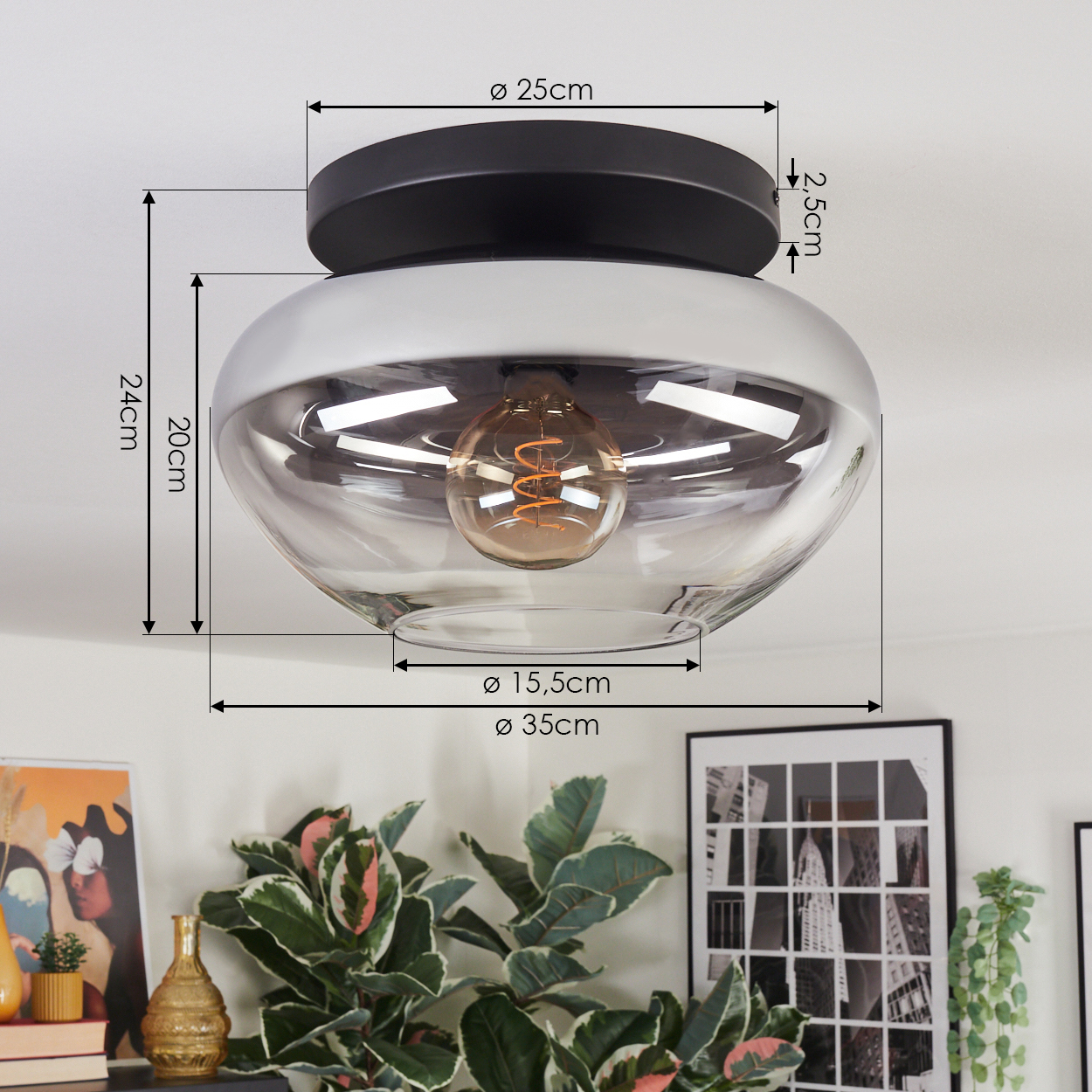 Eine moderne Deckenlampe mit schwarzem Sockel und Glasschirm. Abmessungen sind angezeigt. Pflanzen und Bilder sind im Hintergrund.
