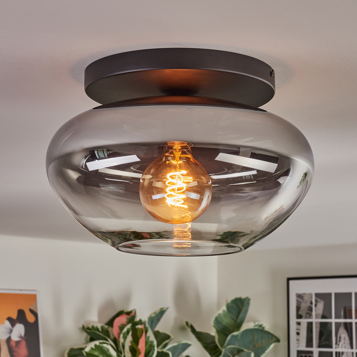 Moderne Deckenleuchte mit Rauchglasschirm und sichtbarer Edison-Glühbirne. Die Leuchte ist an einer weißen Decke montiert.