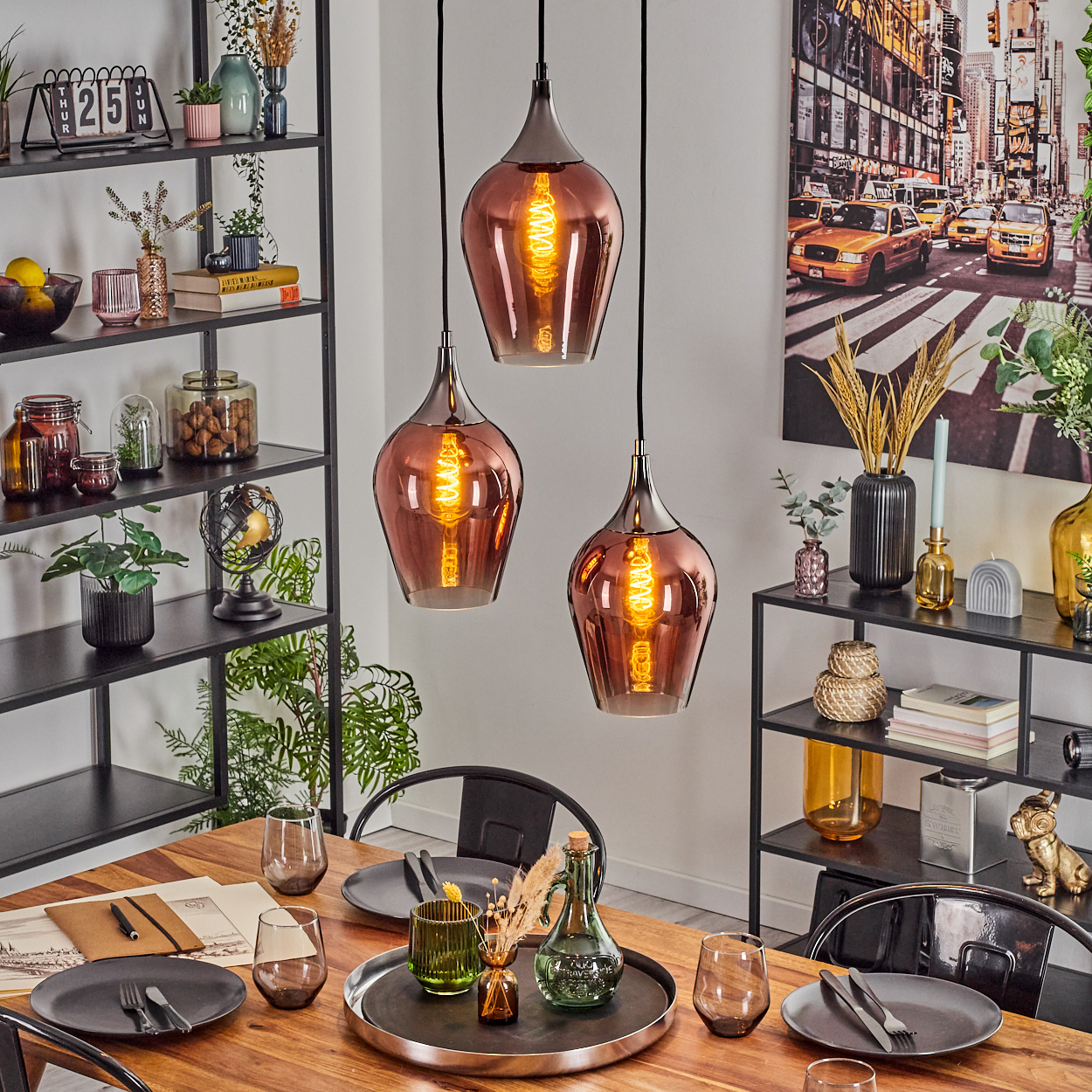 Esszimmer mit Holztisch, Hängelampen und einem Gemälde der Skyline von New York City an der Wand. Zubehör auf Regalen.