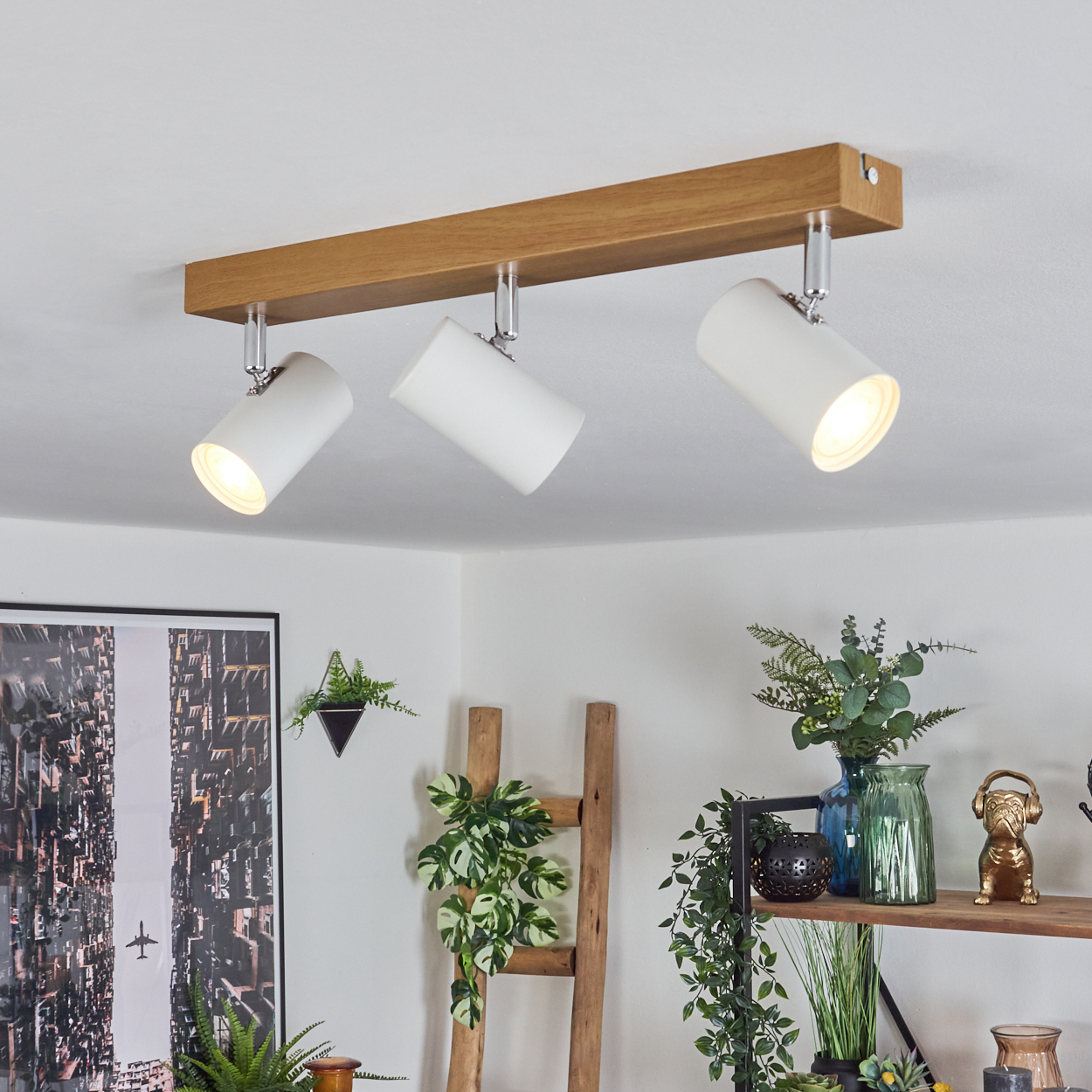 Drei weiße Strahler an einem Holzbalken an der Decke, die einen Raum mit Pflanzen und Dekorationen beleuchten.