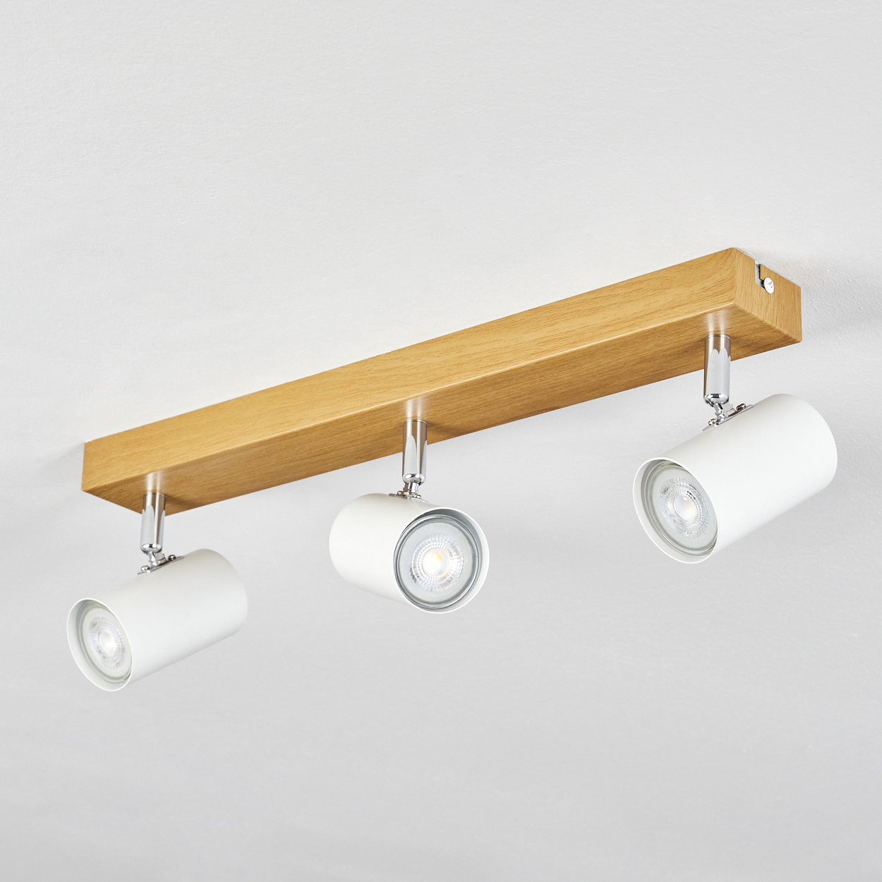 Ein Holzbalken mit drei weißen Strahlern. Die Lichter sind nach unten gerichtet. Die Decke ist weiß.