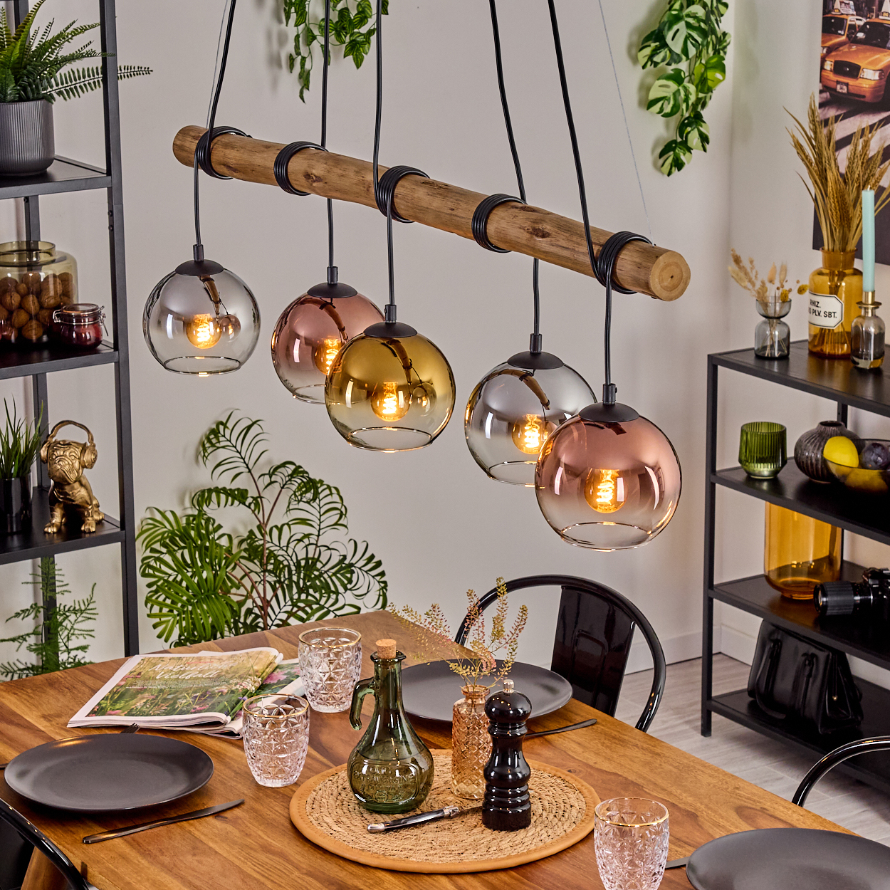 Ein Esszimmer mit Holztisch, Hängelampen und Dekorationen. Auf dem Tisch liegen eine Zeitschrift und Gläser.