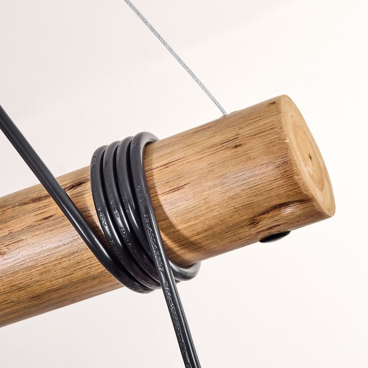 Ein Holzstamm mit schwarzen Drähten. Ein silberner Draht hängt von oben. Der Hintergrund ist weiß.