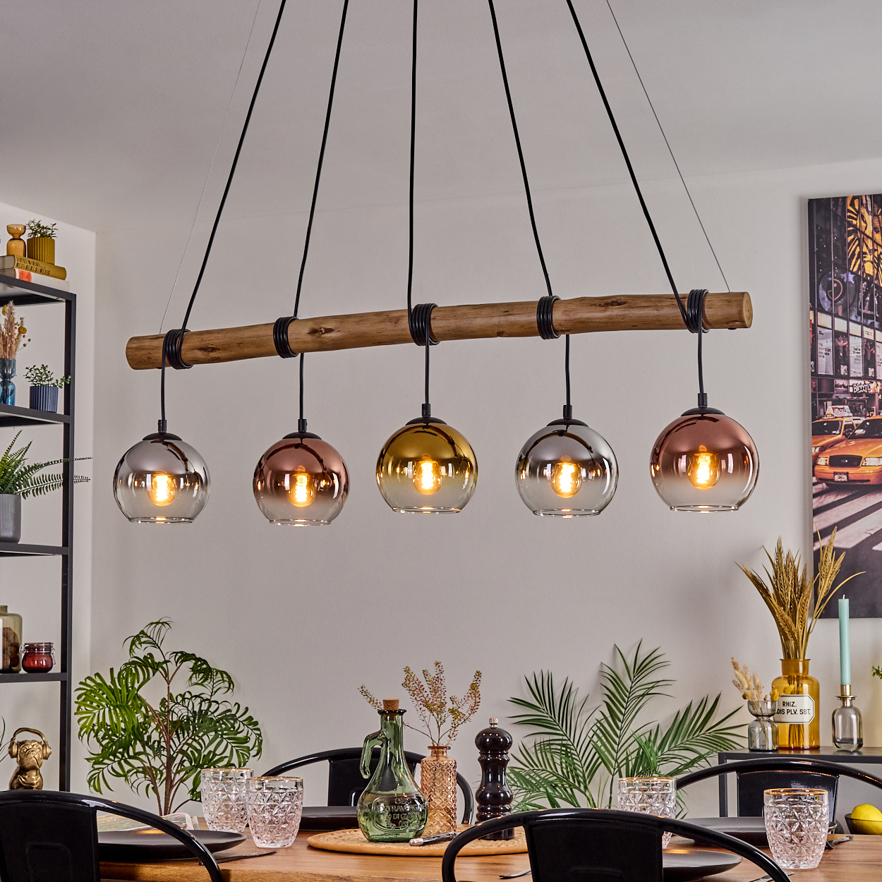 Esszimmer mit Holztisch. Fünf Pendelleuchten hängen darüber. Pflanzen und Dekoration auf dem Tisch und in Regalen, ein Stadtbildgemälde an der Wand.