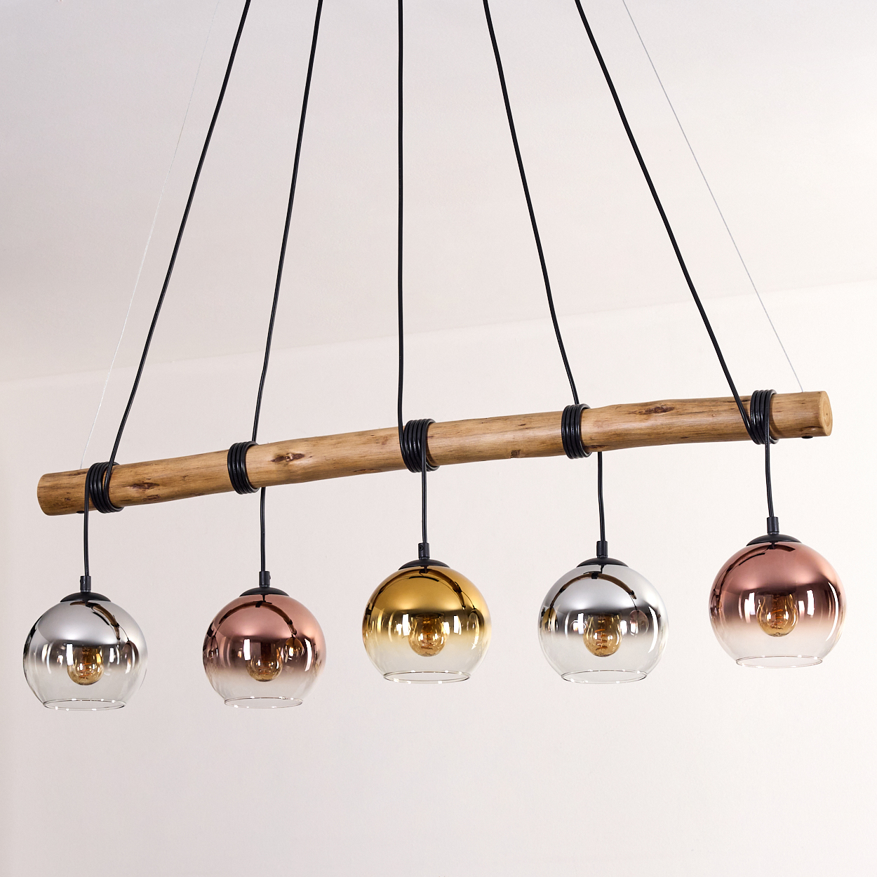 Eine moderne Hängelampe mit fünf kugelförmigen Lampen. Die Lampen haben unterschiedliche Farben: Silber, Kupfer, Gold, Silber und Kupfer. Die Lampen hängen an einem Holzbalken.