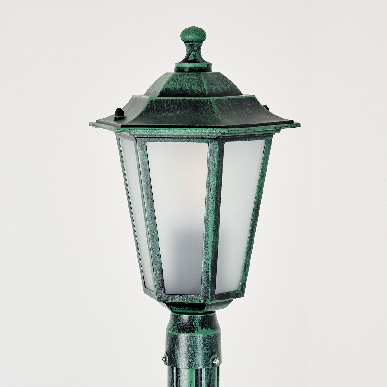 Eine grüne Außenlaterne. Sie hat eine sechseckige Oberseite und Milchglasscheiben. Der Pfosten und die Lampe sind grün mit schwarzen Akzenten.