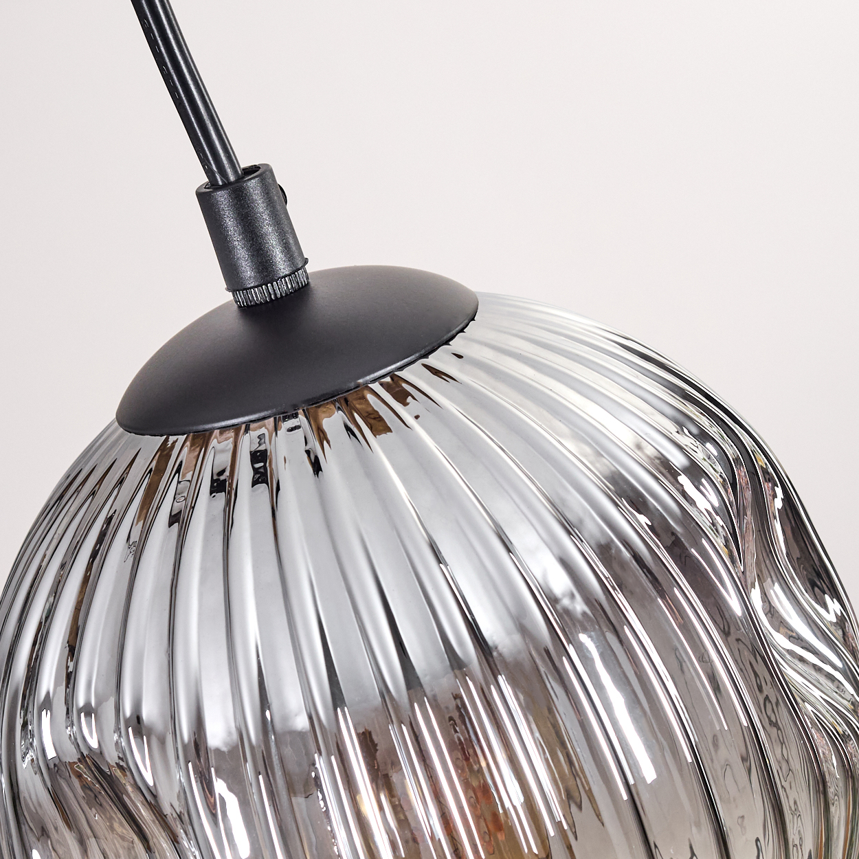 Nahaufnahme einer Glaslampe mit schwarzem Kabel. Die Lampe ist metallisch silberfarben und hat ein geripptes Design.