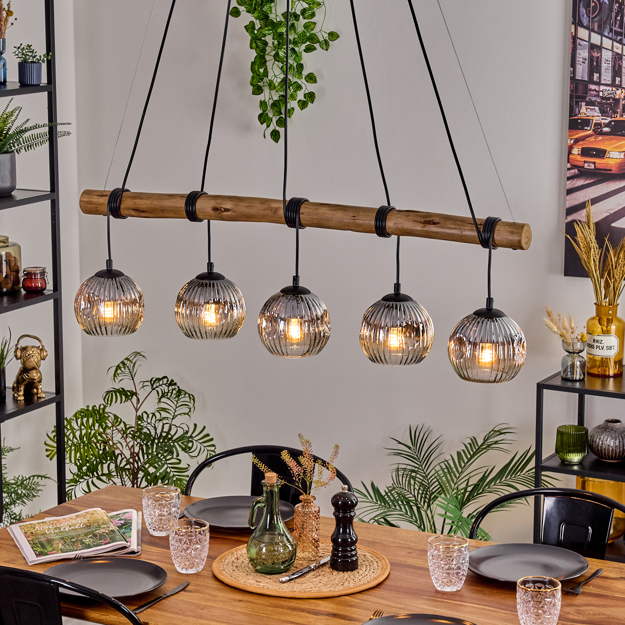 Esszimmer mit Holztisch, Hängelampen, Gläsern, Tellern und Dekorationen. Ein Stadtbildgemälde an der Wand.
