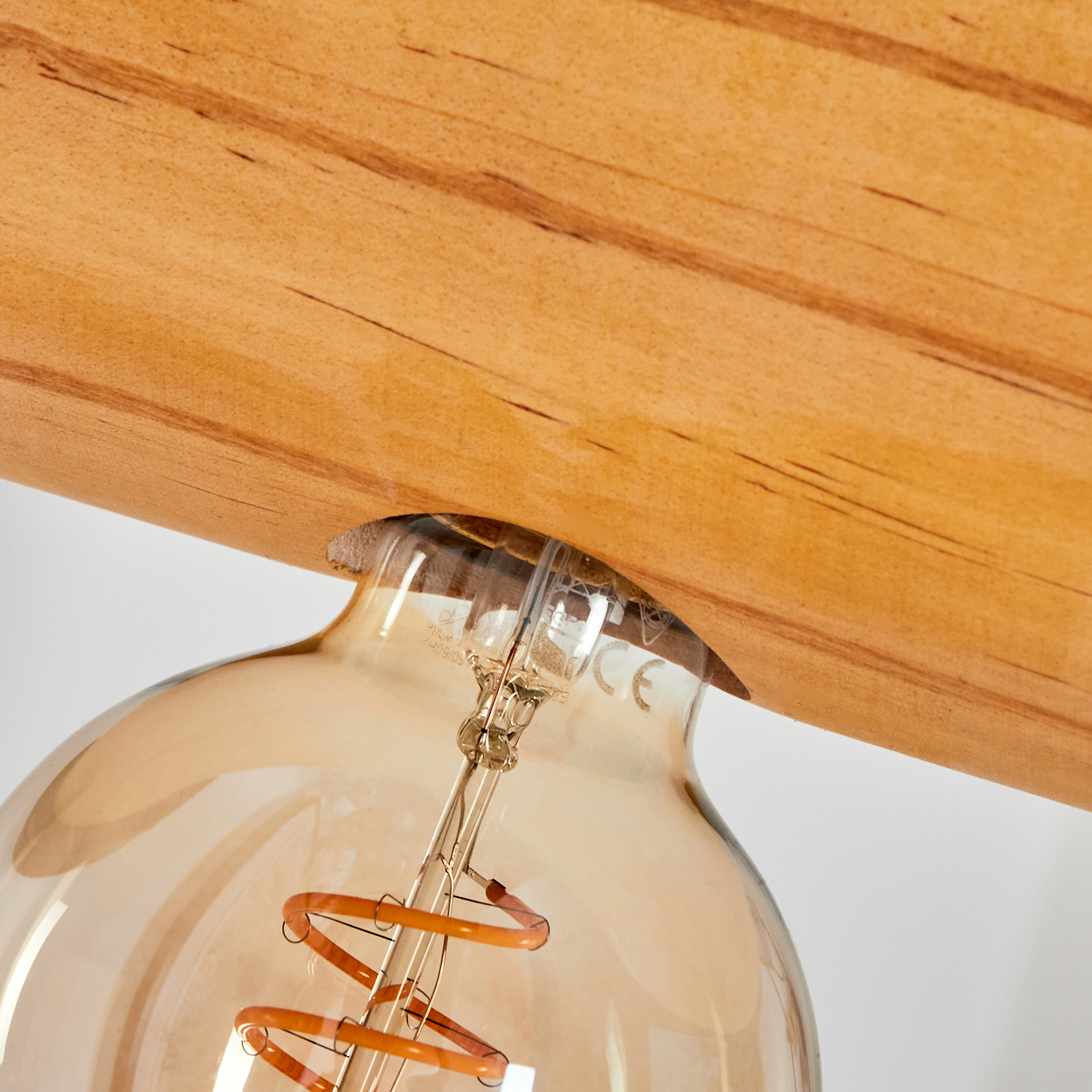 Nahaufnahme einer Glühbirne und eines Holzbalkens. Die Glühbirne ist aus Glas mit einem orangefarbenen Glühfaden.