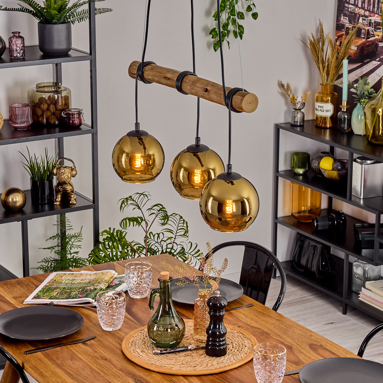 Esszimmer mit Holztisch, drei Pendelleuchten, Regalen mit Deko und einem schwarzen Stuhl. Der Raum ist gut beleuchtet.