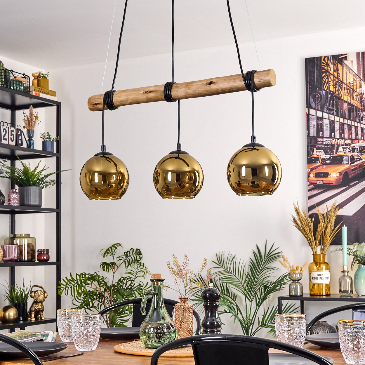 Esszimmer mit Holztisch, goldenen Pendelleuchten, Glaswaren und Pflanzen. Ein New Yorker Straßenkunstwerk an der Wand.
