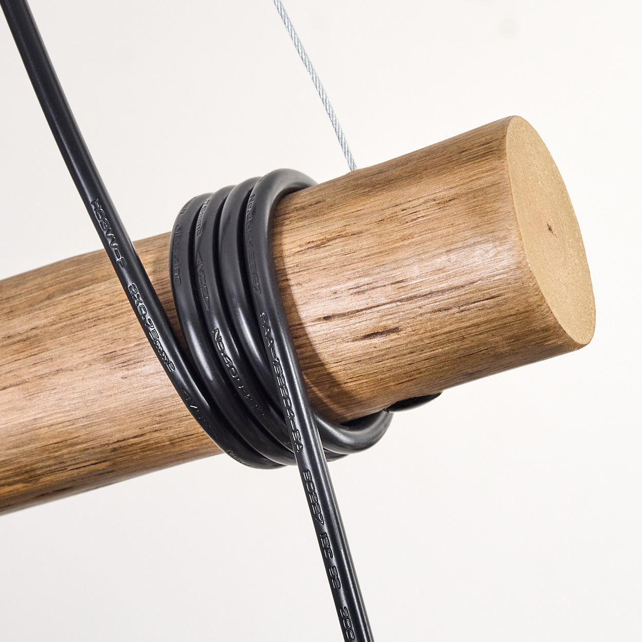 Nahaufnahme eines Holzbalkens mit schwarzen Kabeln. Ein dünner Metalldraht darüber. Der Hintergrund ist weiß.