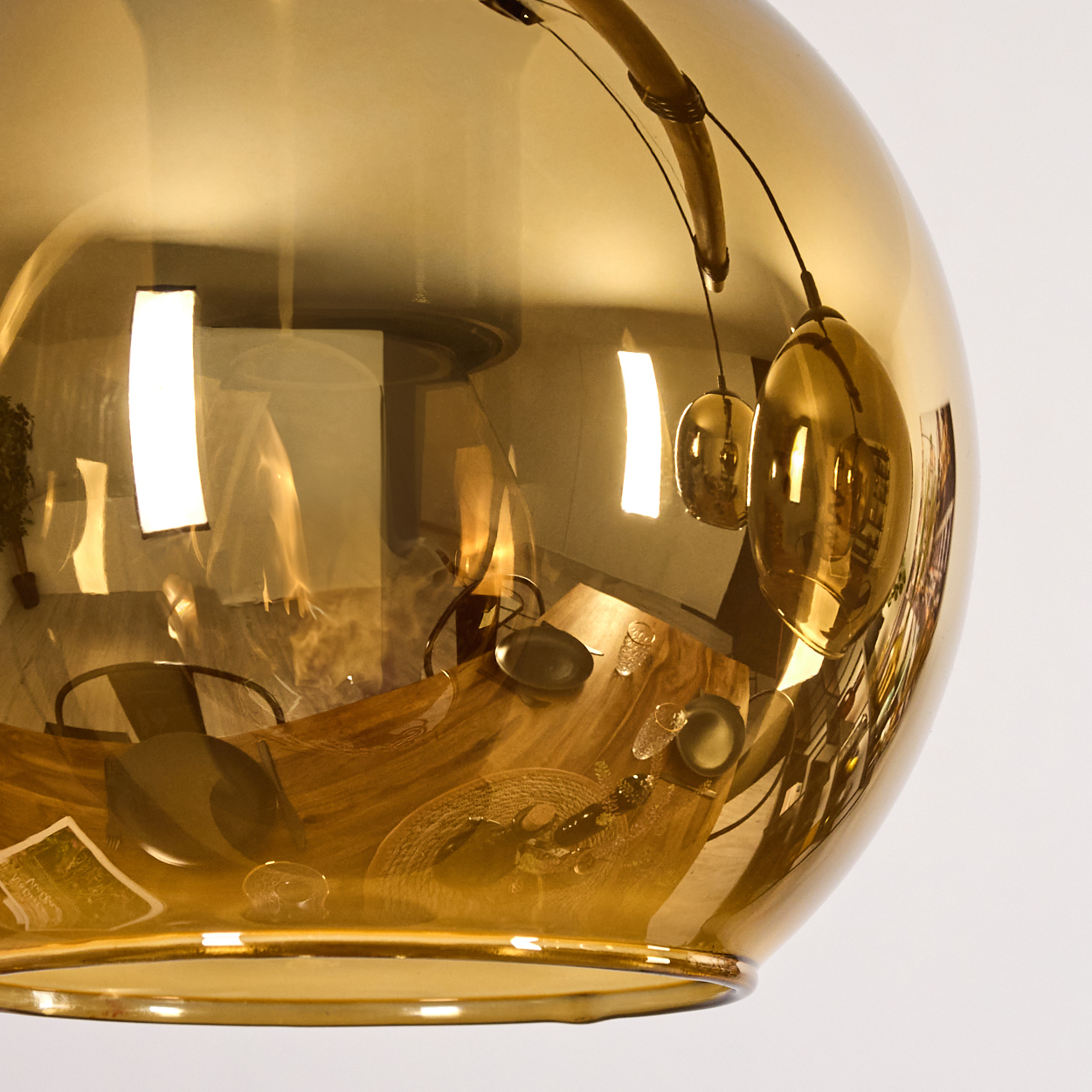 Eine goldene, kugelförmige Lampe reflektiert eine Esszene. Ein Holztisch mit Tellern, Gläsern und ein Fenster sind sichtbar.