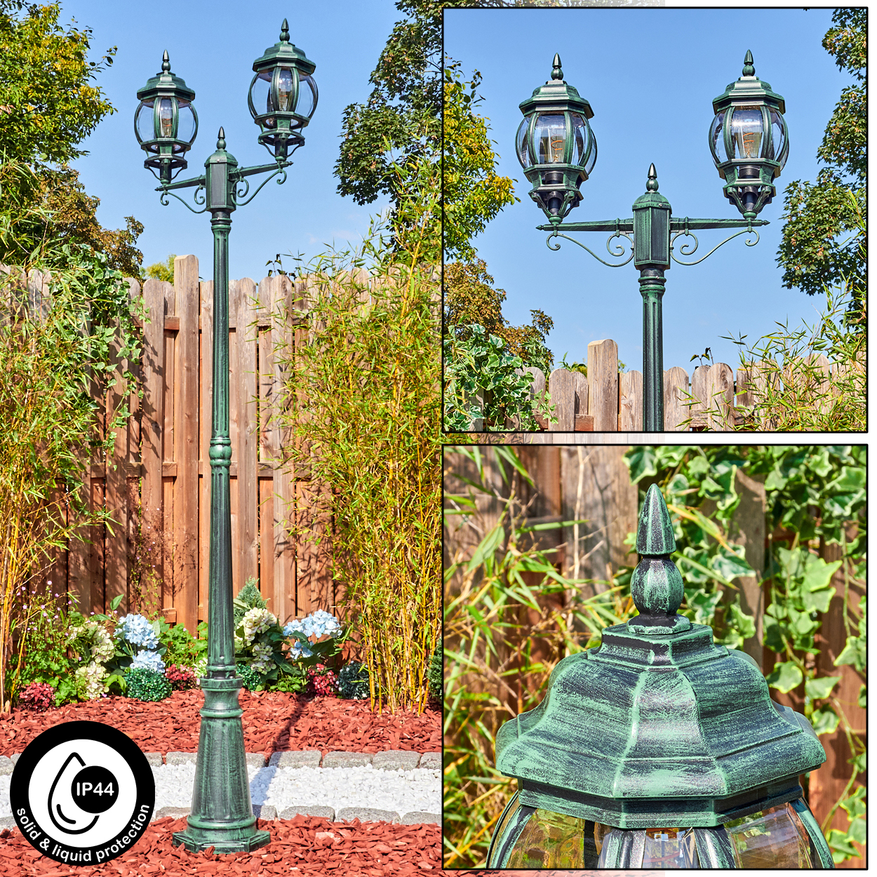 Eine grüne Laterne mit drei Lampen, die in einem Garten mit Holzzaun und Pflanzen im Hintergrund steht.