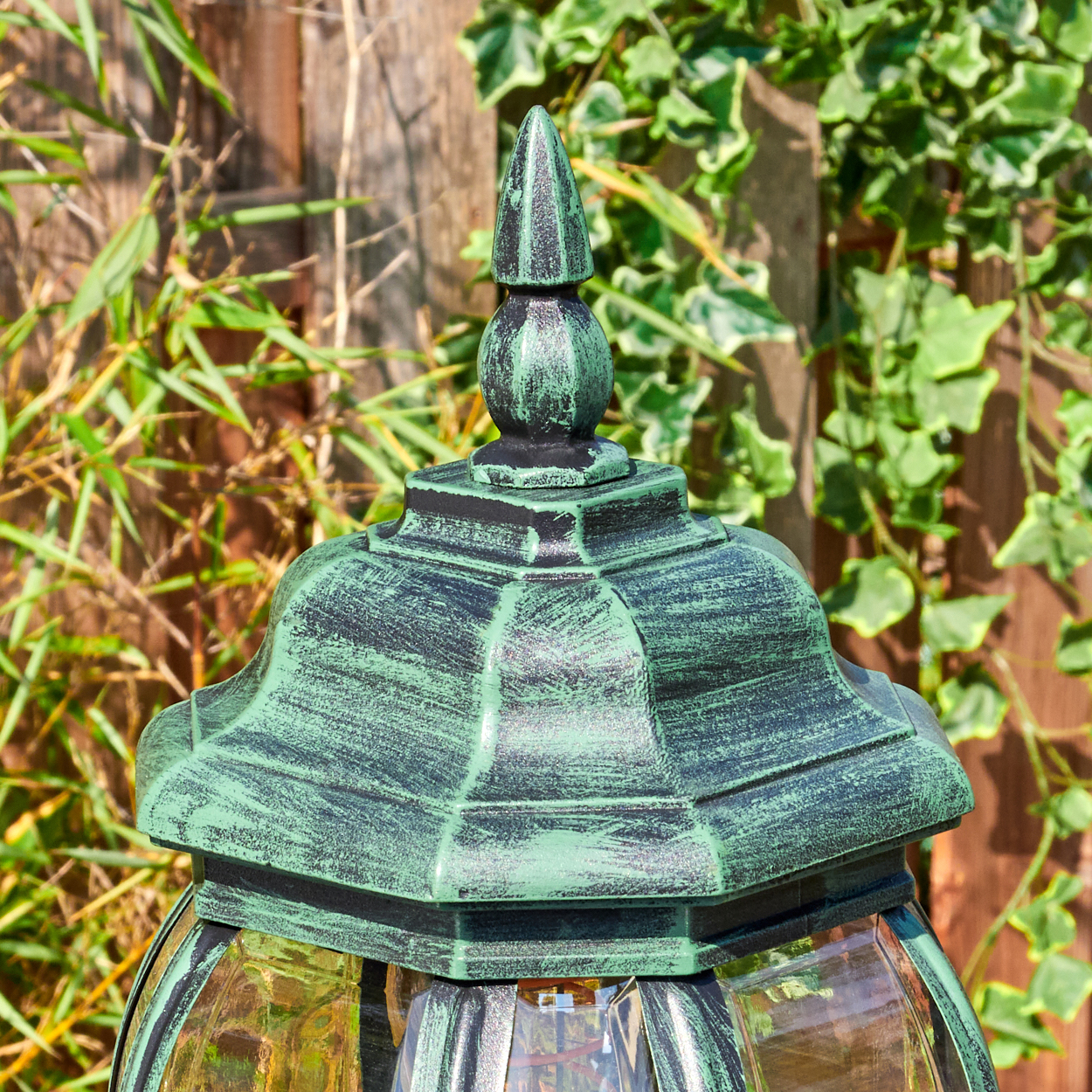Nahaufnahme einer grün-schwarzen Außenlampe mit Glaskugel. Efeu und ein Holzzaun sind im Hintergrund.