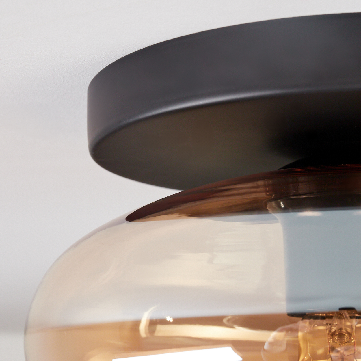 Nahaufnahme einer modernen Deckenleuchte. Sie hat einen schwarzen Metallsockel und einen braun getönten Glasschirm, mit einer sichtbaren Glühbirne.