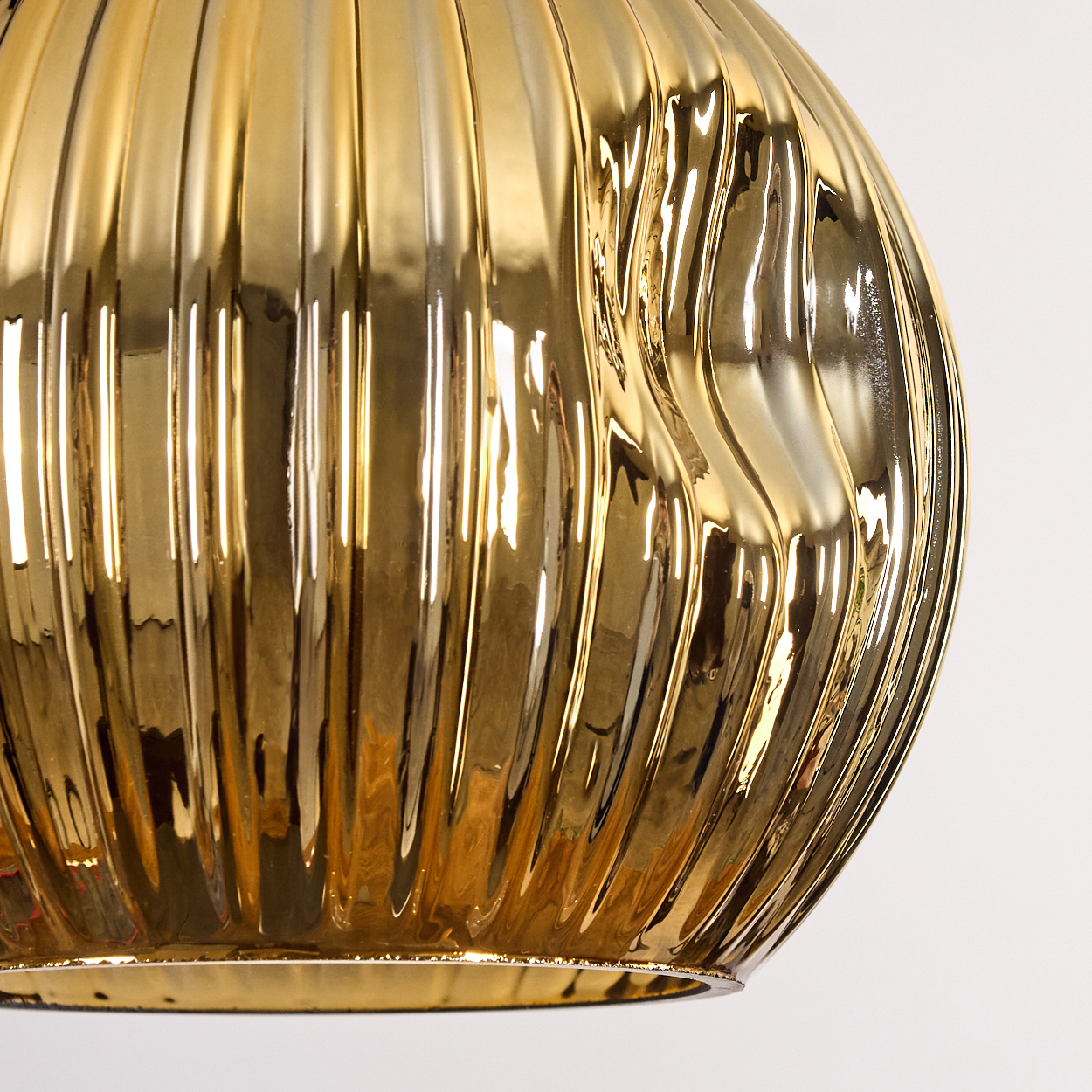 Nahaufnahme eines goldenen, gerippten Glasobjekts vor weißem Hintergrund. Das Glas reflektiert Licht und hat eine glänzende Textur.