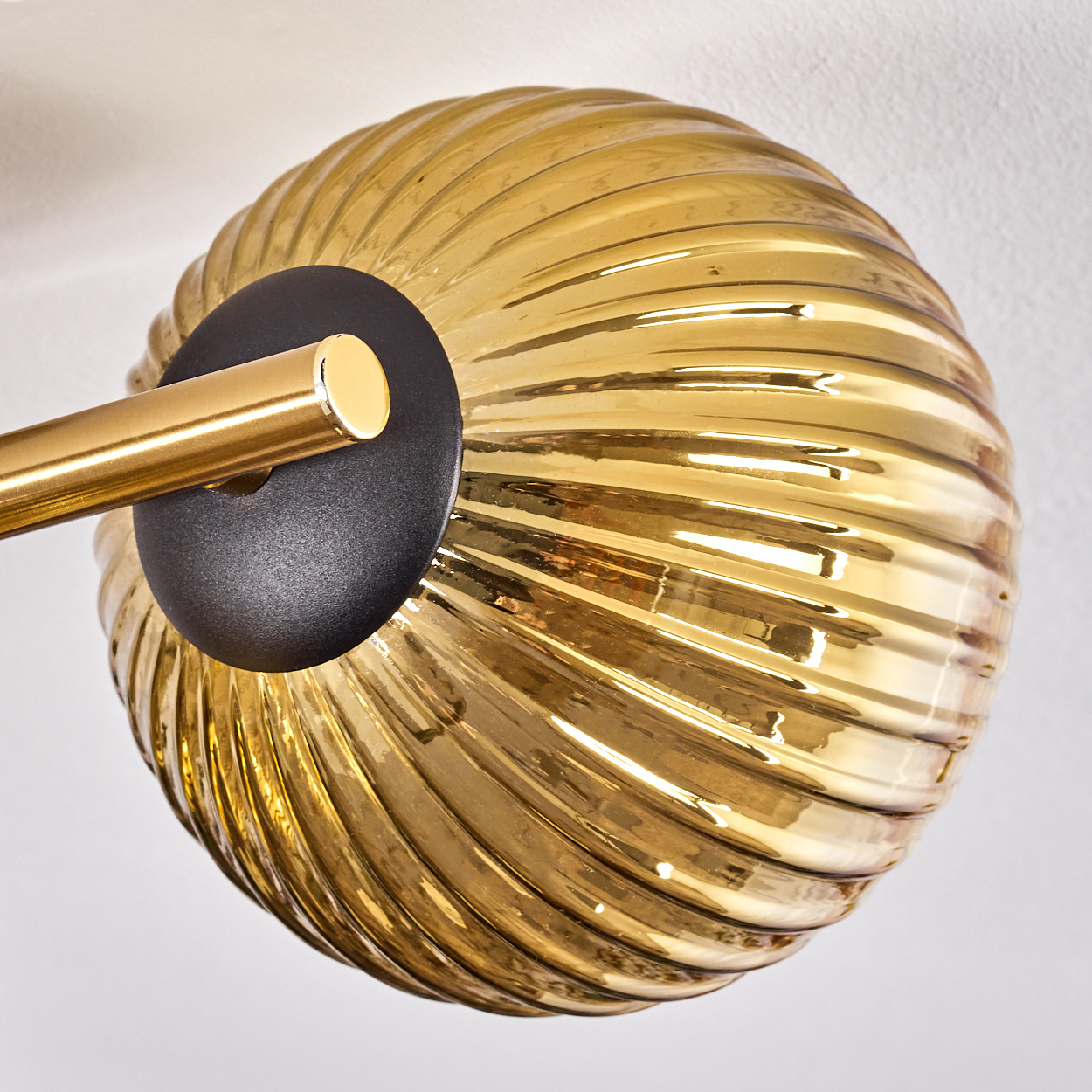 Nahaufnahme einer modernen Leuchte. Sie hat einen runden, gerippten, bernsteinfarbenen Glasschirm, einen schwarzen Sockel und einen goldenen Arm.