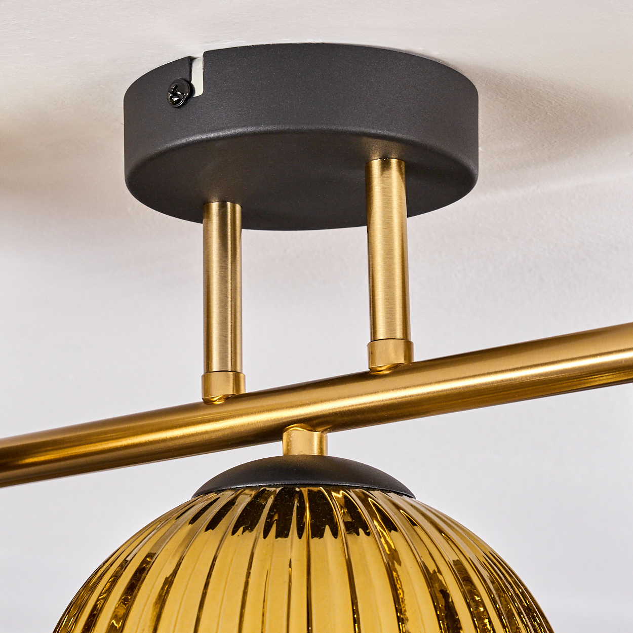 Nahaufnahme einer modernen Leuchte. Sie hat einen schwarzen, kreisförmigen Sockel, goldene Stäbe und einen gerippten, goldfarbenen Glasschirm.