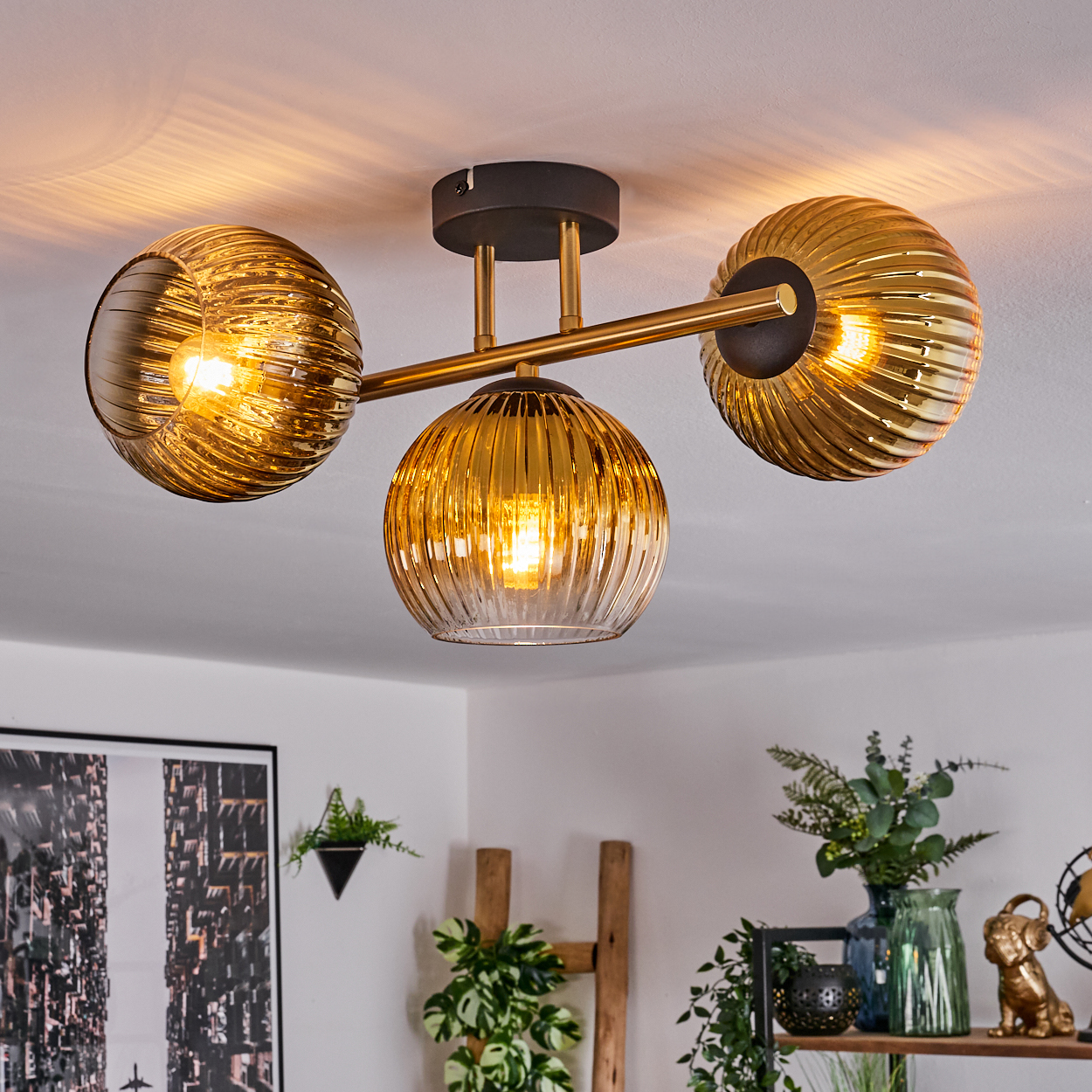 Deckenleuchte mit drei goldenen Glaskugeln, jede mit einer Glühbirne. Im Hintergrund sind weiße Decke und Dekoration zu sehen.