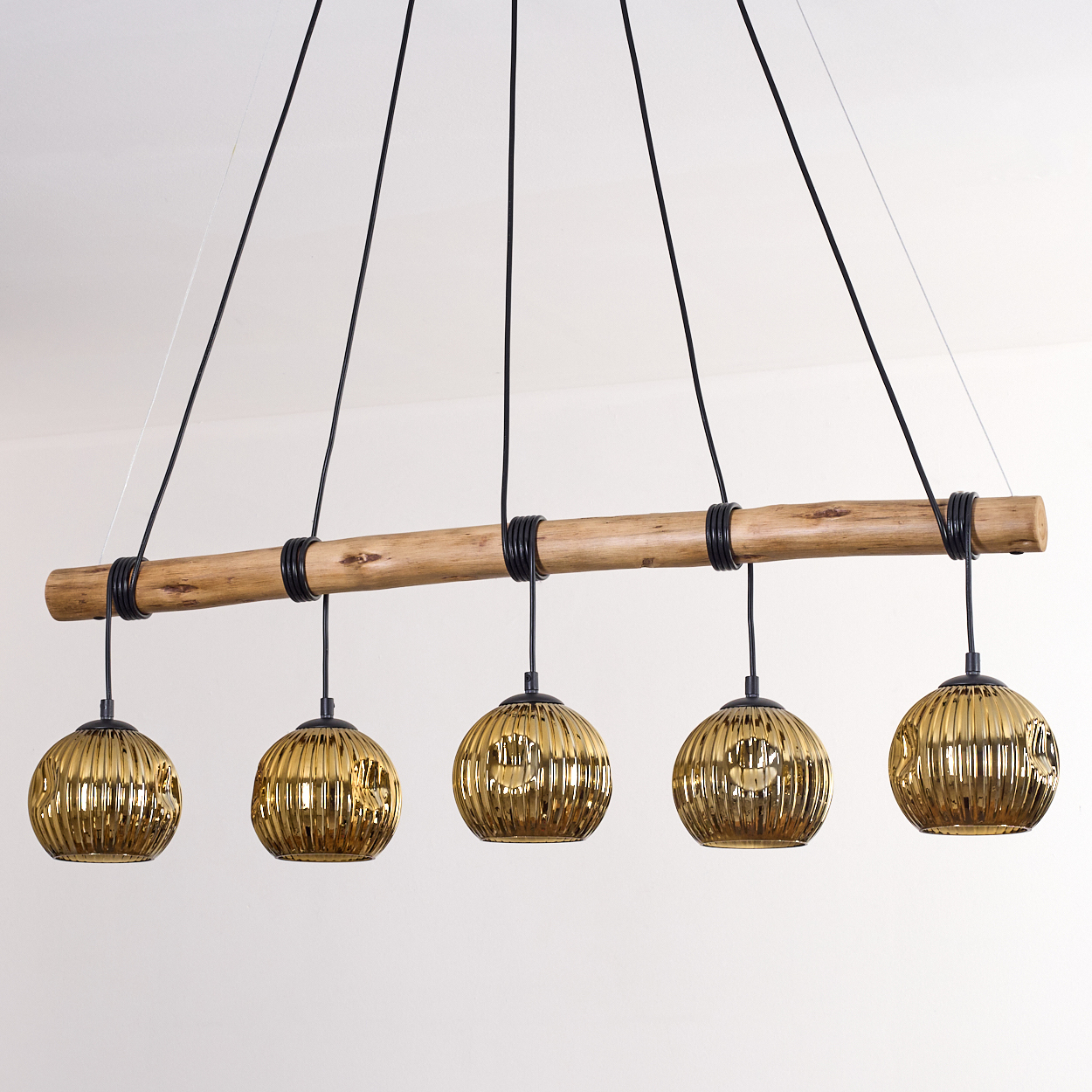 Ein moderner Kronleuchter mit fünf goldenen Glaskugellampen, die an einem Holzbalken hängen.
