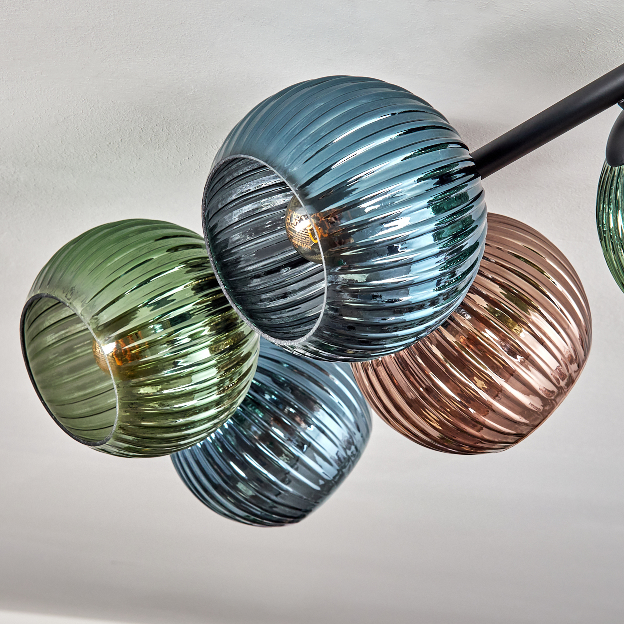 Eine moderne Deckenleuchte mit mehreren kugelförmigen, gewirbelten Glasschirmen in verschiedenen Farben: Grün, Blau und Kupfer. Der Hintergrund ist weiß.