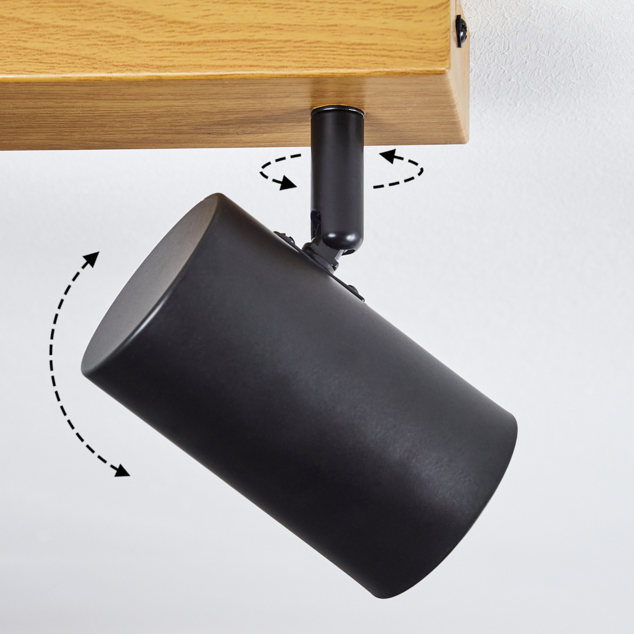 Ein schwarzer Strahler ist an einem Holzbalken befestigt. Pfeile zeigen den einstellbaren Bereich des Strahlers an. Der Hintergrund ist eine weiße Wand.