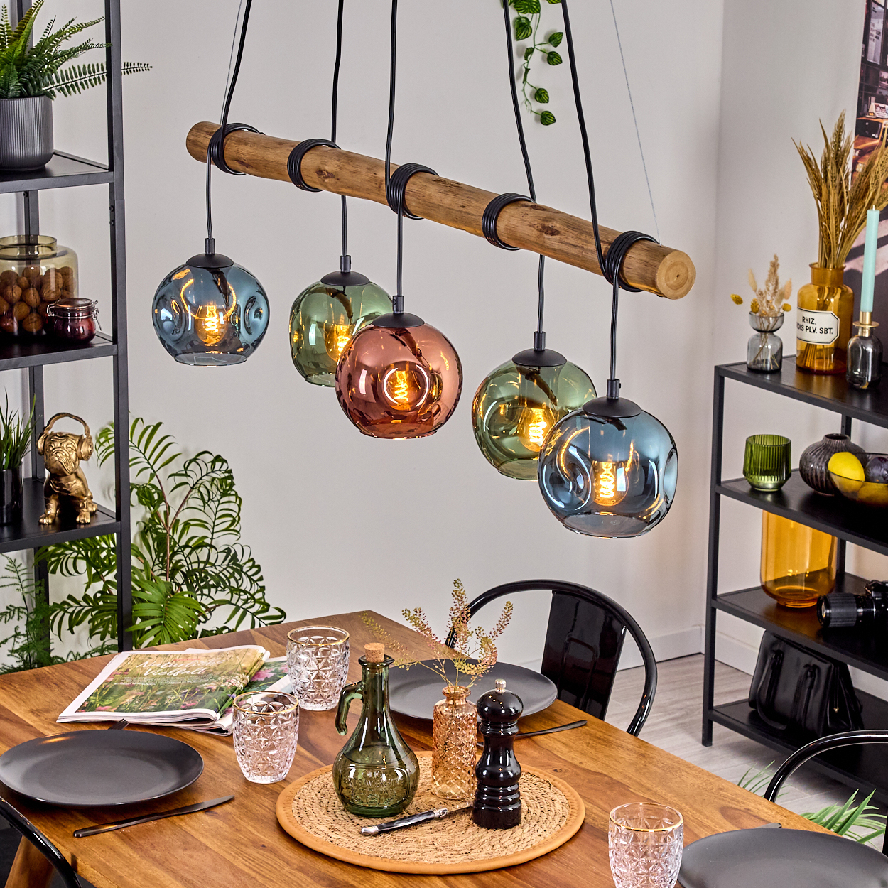 Ein Esszimmer mit Holztisch, Leuchte mit farbigen Glaskugeln und dekorativen Gegenständen.