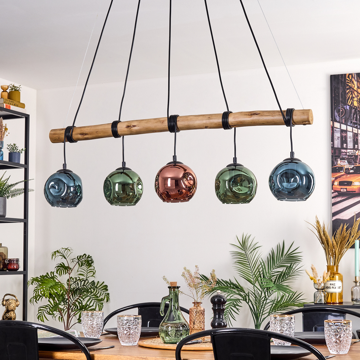 Ein Esszimmer mit Holztisch. Eine Leuchte mit fünf bunten Glaskugeln hängt darüber. Pflanzen und Dekoration sind ebenfalls sichtbar.