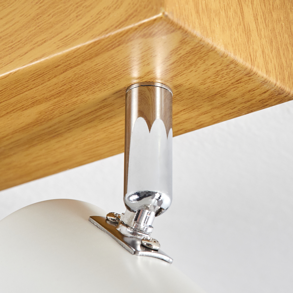 Nahaufnahme einer Deckenleuchte. Sie hat einen Holzsockel, einen Chromarm und ein weißes, abgerundetes Licht. Der Hintergrund ist weiß.