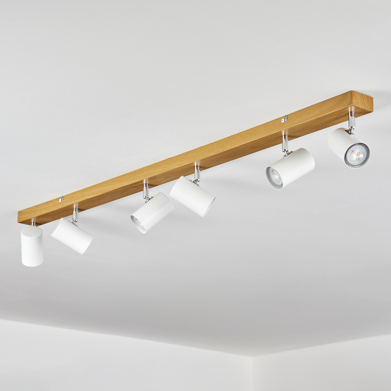 Ein Holzbalken mit sechs weißen Strahlern an einer weißen Decke. Die Lichter sind nach unten geneigt.