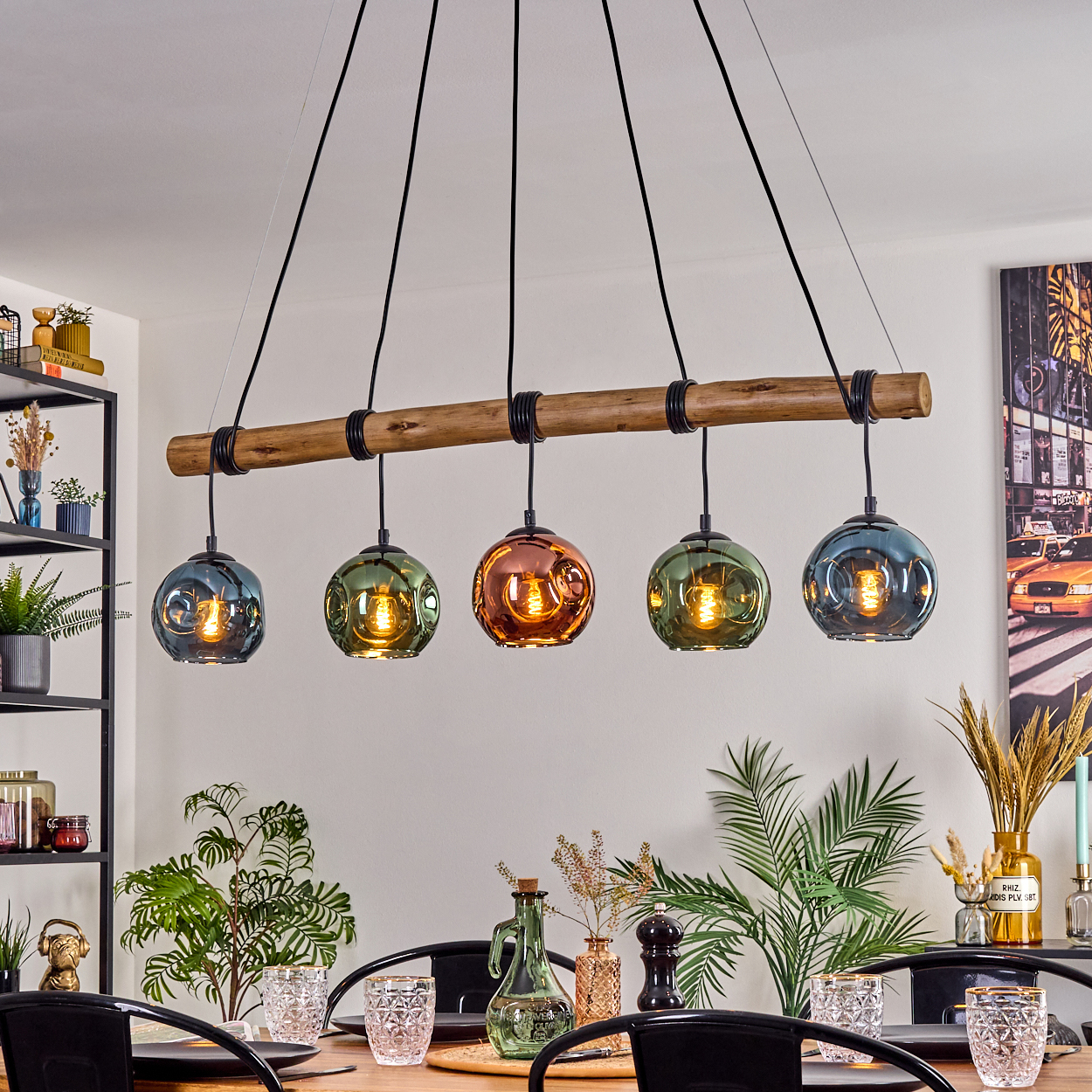 Ein Esszimmer mit einem Holzbalken-Kronleuchter. Fünf Glas-Kugelleuchten in verschiedenen Farben hängen über dem Tisch. Pflanzen und Dekoration sind ebenfalls vorhanden.