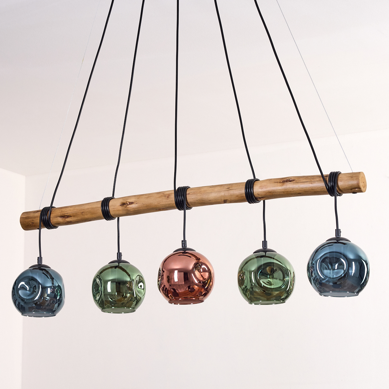 Eine moderne Hängelampe mit fünf kugelförmigen Glasschirmen in Blau, Grün und Kupfer. Sie hängt an einem Holzbalken.