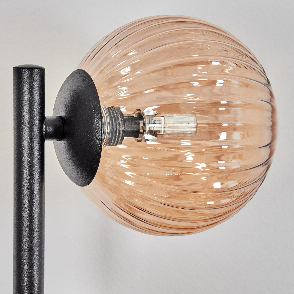 Nahaufnahme einer Lampe. Sie hat einen schwarzen Metallsockel und einen hellbraunen Glaskolben mit gerilltem Design. Der Hintergrund ist weiß.
