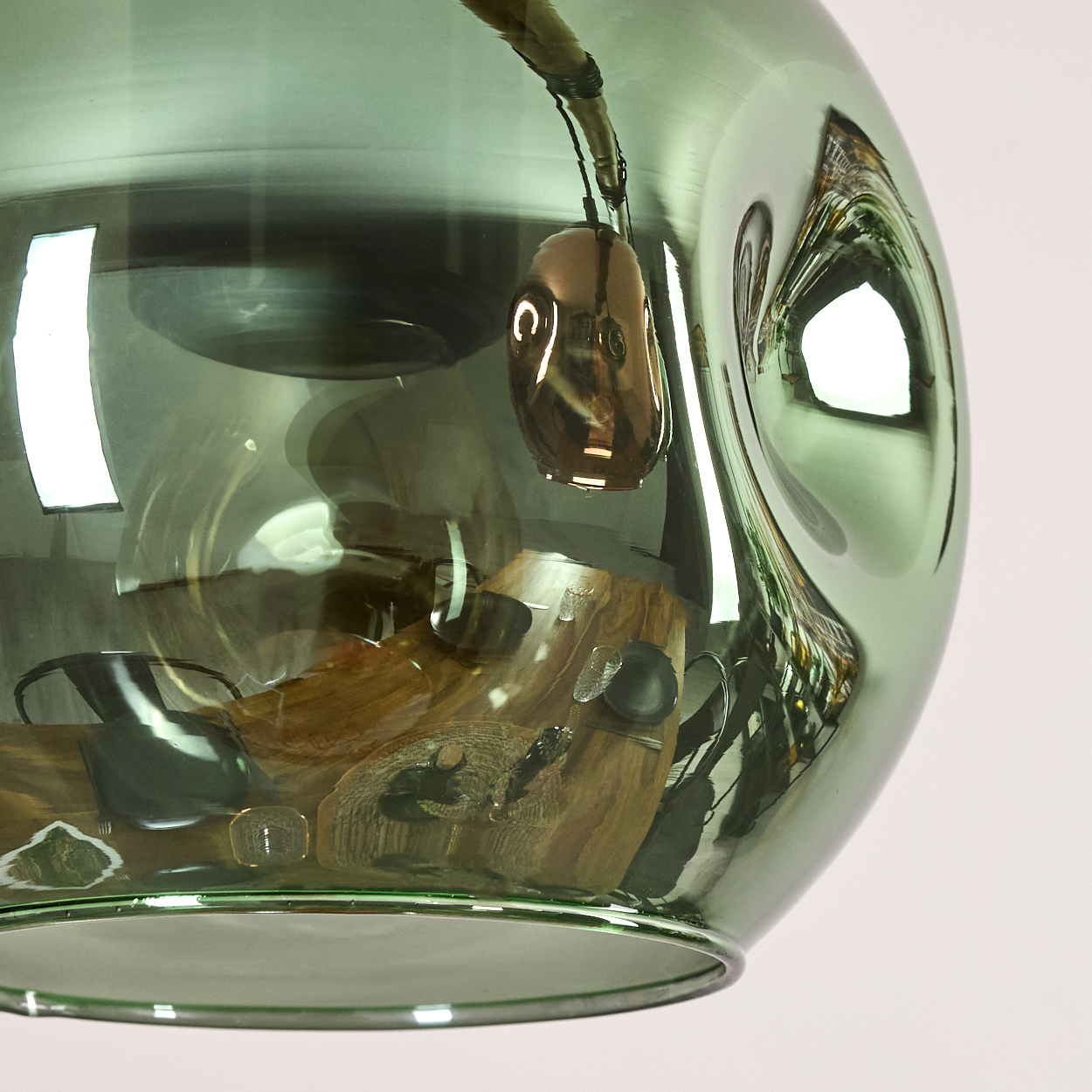 Eine grüne Glaspendelleuchte reflektiert eine Holzoberfläche mit Objekten. Ein bronzefarbenes Element hängt im Glas.