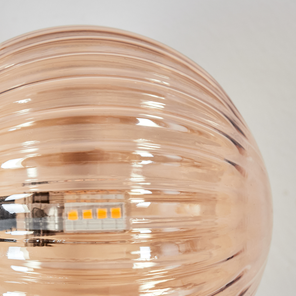 Nahaufnahme einer Leuchte. Sie hat eine geriffelte, pfirsichfarbene Glaskuppel. Im Inneren befindet sich eine LED-Leuchte.