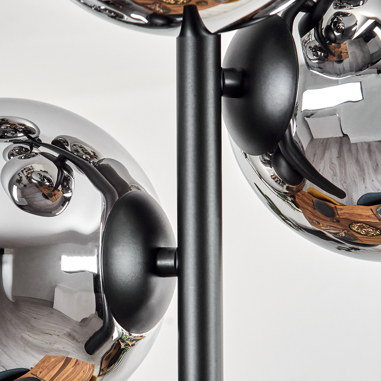 Nahaufnahme einer modernen Lampe mit verchromten Kugeln, die den Raum reflektieren. Schwarze Halterungen halten die Kugeln.
