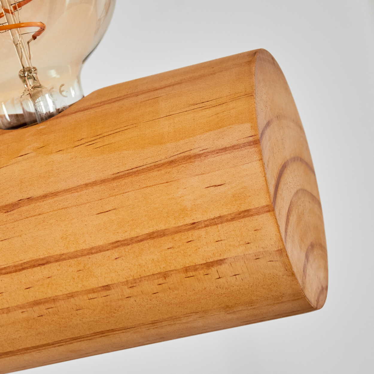 Nahaufnahme eines Holzbalkens, der eine Glühbirne trägt. Der Balken ist hellbraun mit sichtbarer Holzmaserung. Die Glühbirne ist aus Glas.