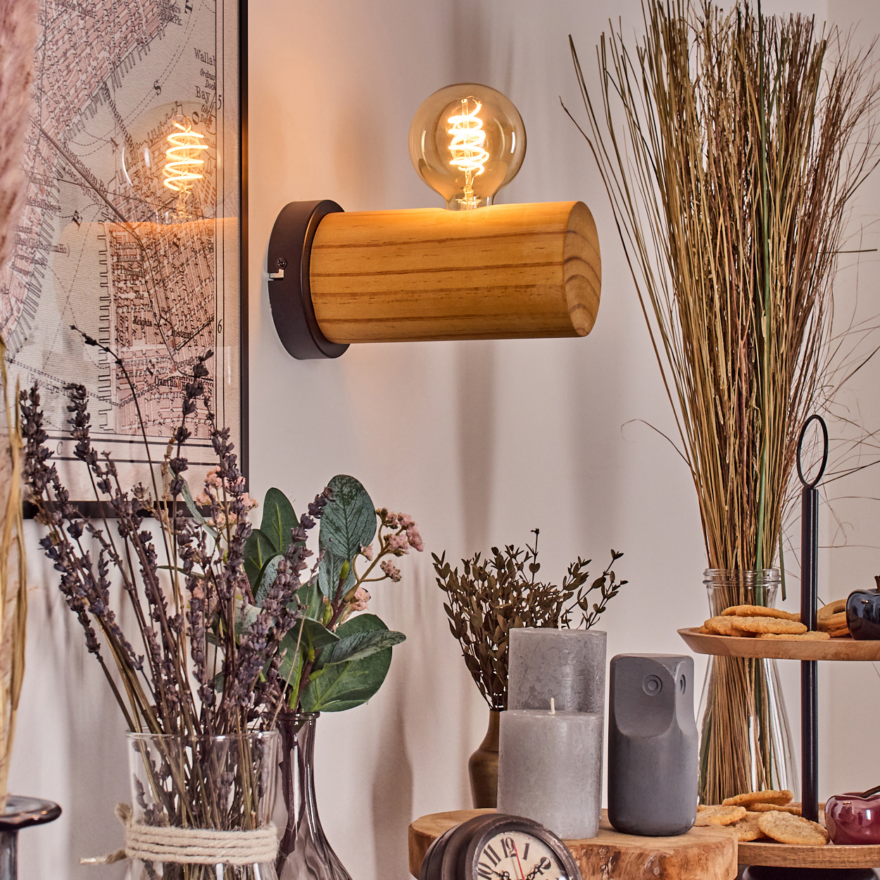 Ein Raum mit einer hölzernen Lampe, Blumen, Kerzen, Keksen und einer Karte. Die Wand ist weiß. Das Licht ist warm.