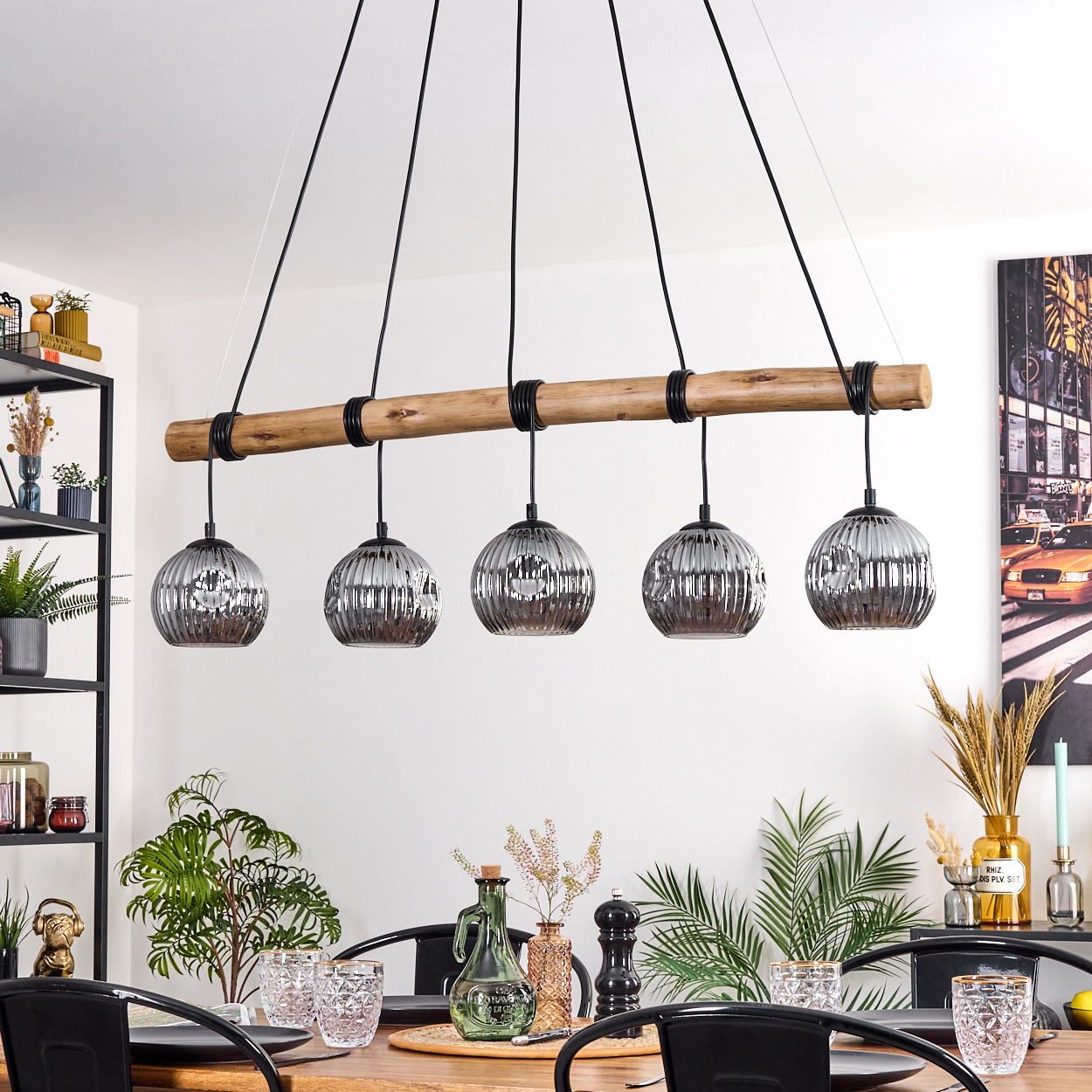 Ein Esszimmer mit Holztisch, schwarzen Stühlen und einem Kronleuchter mit fünf Kugelleuchten. Pflanzen und Dekorationen sind vorhanden.