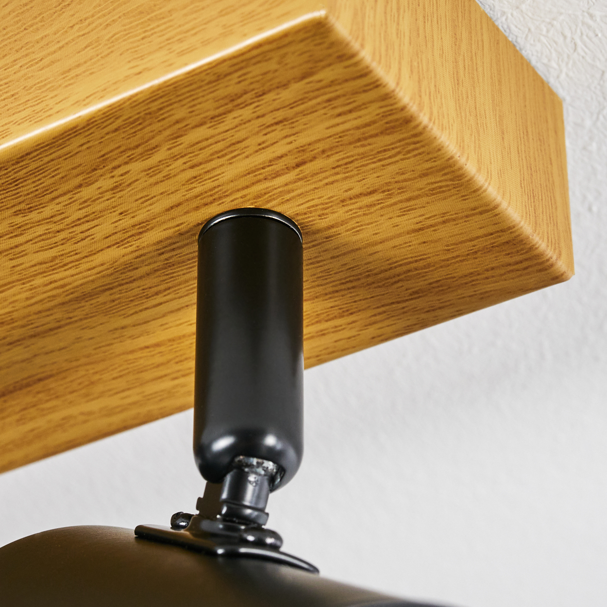 Nahaufnahme einer Deckenleuchte. Ein Holzbalken ist an der Decke befestigt, darunter hängt eine schwarze zylindrische Leuchte.