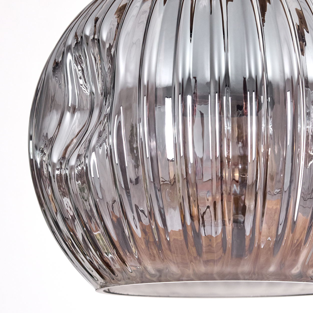Nahaufnahme einer klaren Glasvase mit vertikalen Rippen. Die Vase reflektiert Licht und eine Holzoberfläche. Weißer Hintergrund.