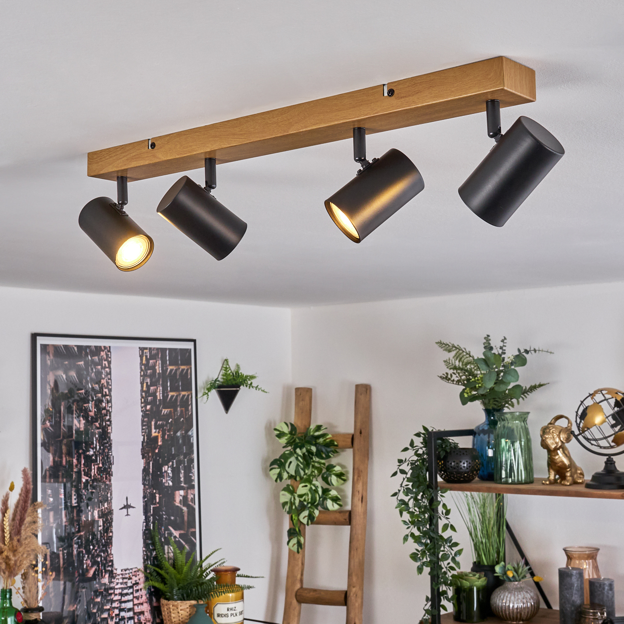 Deckenstrahler auf einem Holzbalken. Pflanzen, Bilder und Dekorationen auf Regalen im Hintergrund. Der Raum hat weiße Wände.