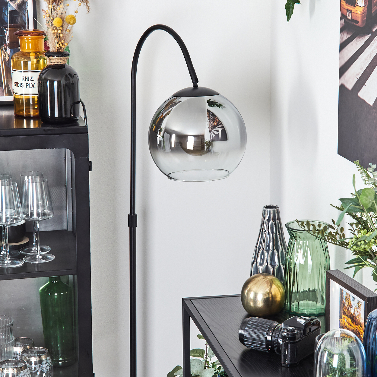 Ein modernes Interieur mit schwarzer Lampe, Glasvasen und Kamera. Die Lampe hat einen großen, reflektierenden Kugelschirm.