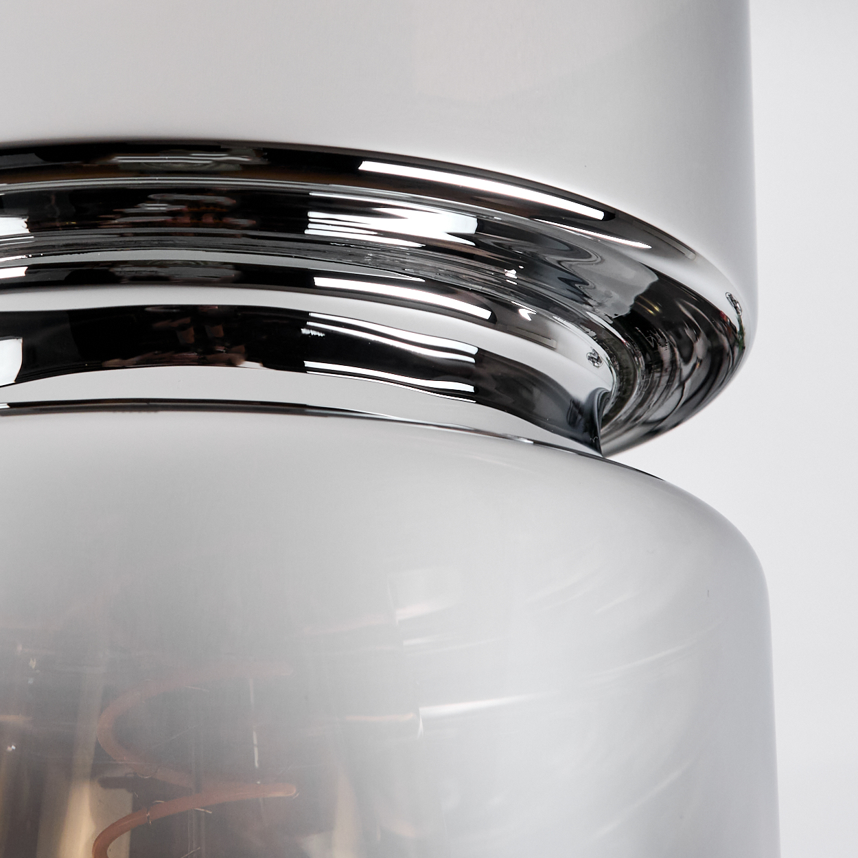 Nahaufnahme einer modernen Lampe. Sie hat einen Chromring zwischen zwei weißen, abgerundeten Glasteilen. Der Hintergrund ist weiß.