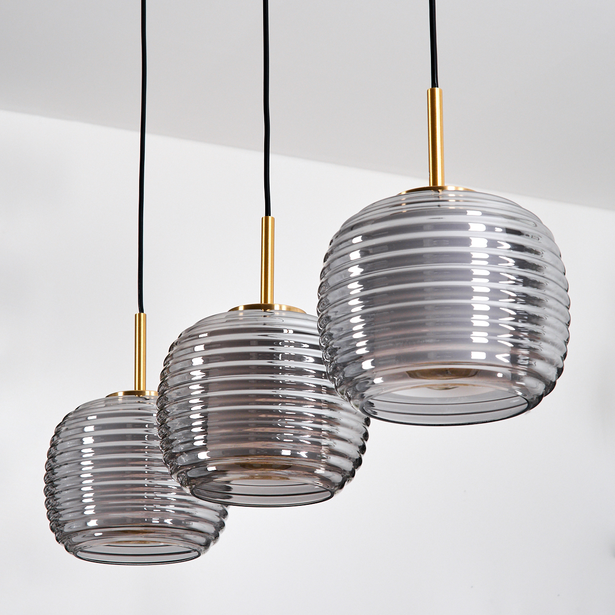 Drei Pendelleuchten mit gerippten Glasschirmen, goldenen Akzenten und schwarzen Kabeln vor weißem Hintergrund.