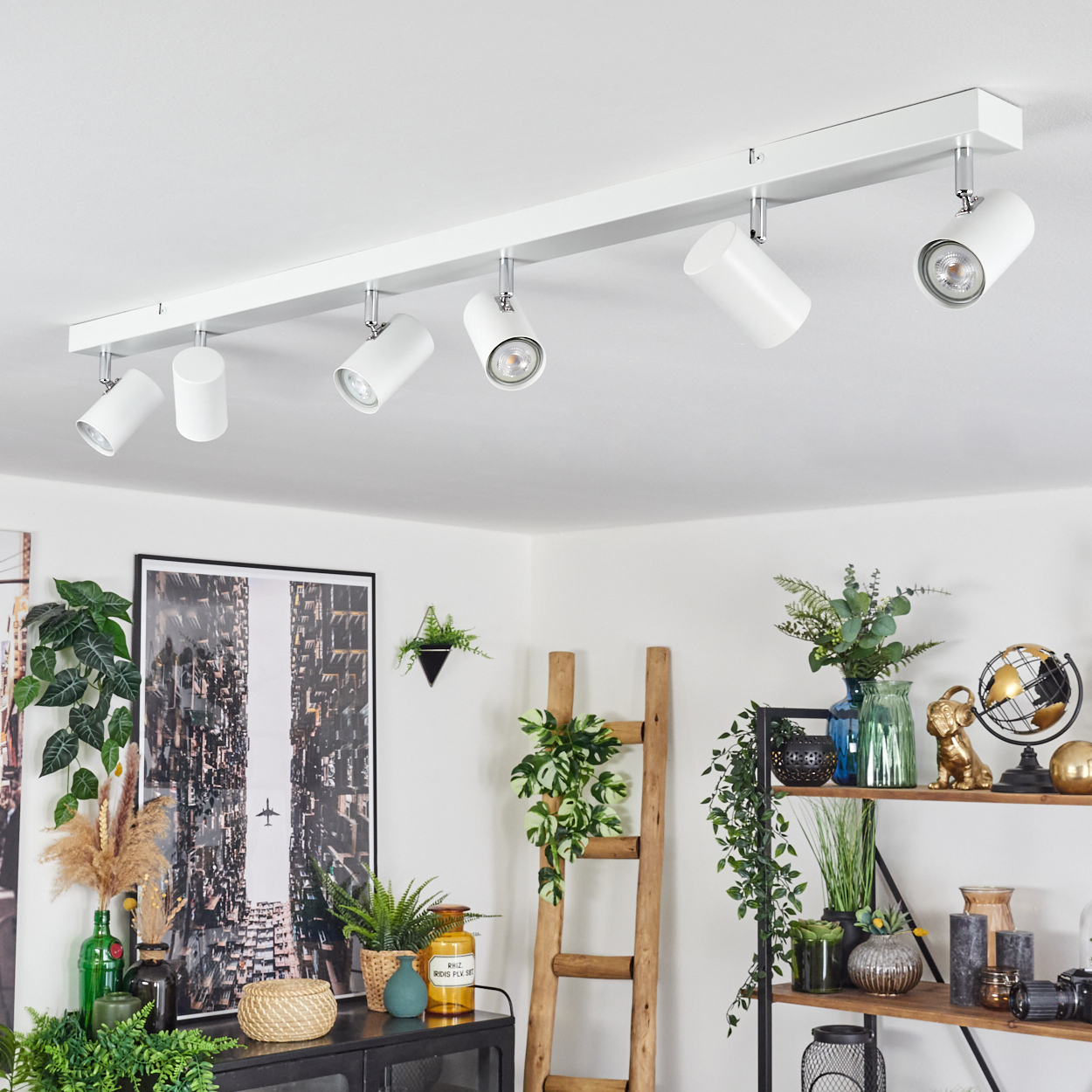 Weiße Deckenstrahler beleuchten einen Raum mit Pflanzen, Kunstwerken und Regalen voller Dekorationen.