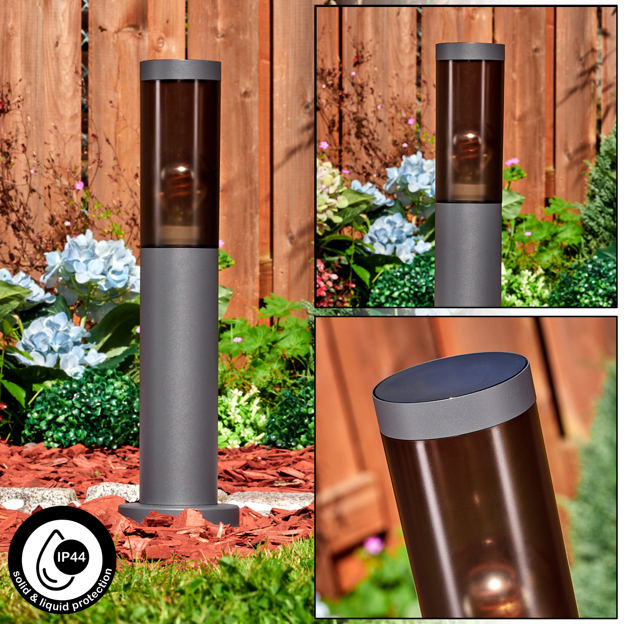 Eine graue Außenlampe mit braun getönter Glasabdeckung steht in einem Garten. Im Hintergrund Blumen und ein Holzzaun.